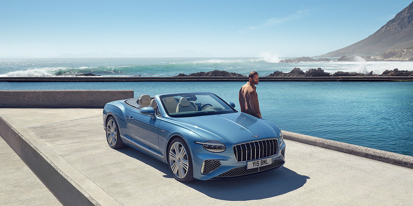 Bentley Johannesburg New Bentley Continental GTC Azure convertible front view in Light Windsor blue paint with 22 inch ten spoke wheels parked by the sea in the sunshine
