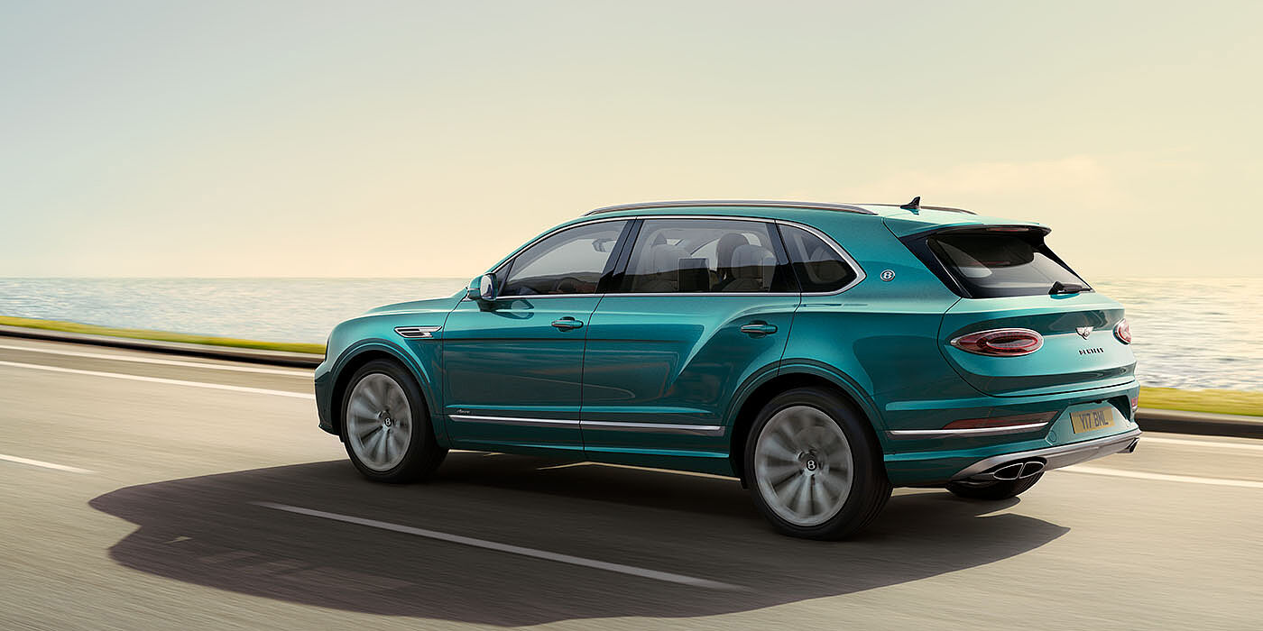 Bentley Johannesburg Bentley Bentayga Extended Wheelbase Azure luxury SUV rear three quarter in Topaz Blue by Mulliner paint, driving on an ocean road.