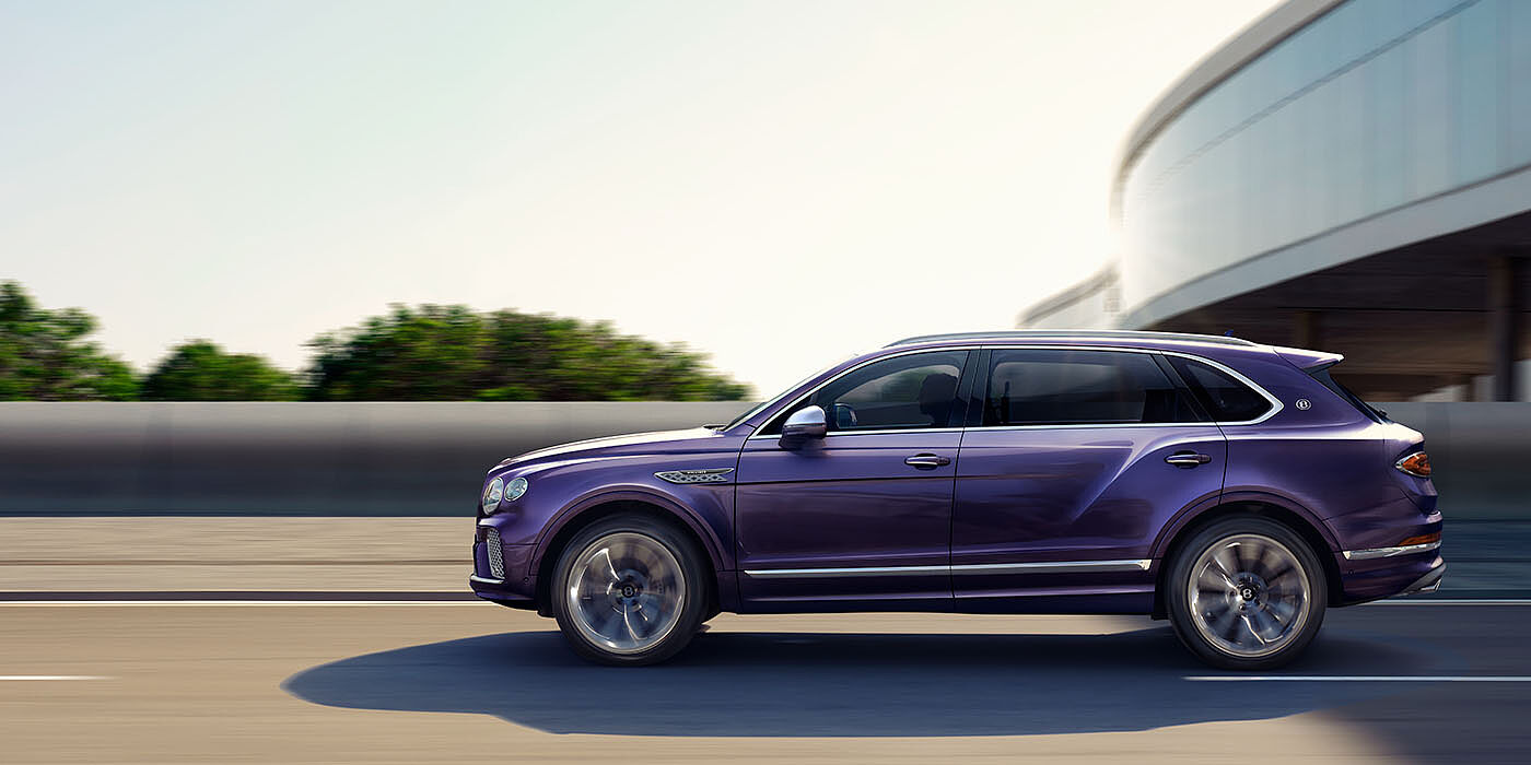 Bentley Johannesburg Bentley Bentayga Extended Wheelbase Mulliner luxury SUV profile in Tanzanite Purple paint, driving on an country road past trees.