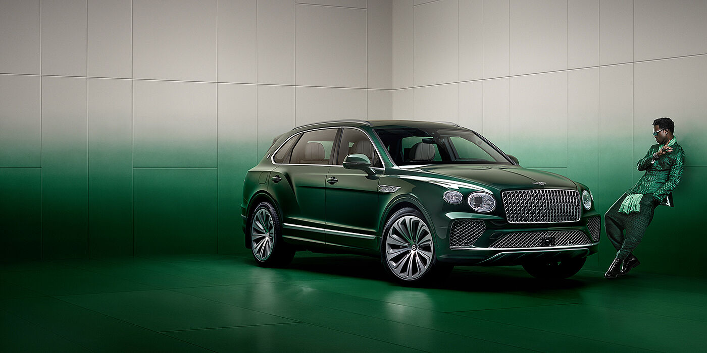 Bentley Johannesburg Wisdom K leans against wall next to Bentley Bentayga Extended Wheelbase Atelier Edition SUV in Light Emerald green paint