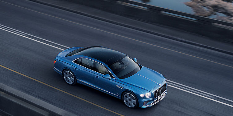 Bentley Johannesburg New Bentley Flying Spur Azure sedan in Light windsor blue paint by Mulliner, with 22 inch Azure wheels seen from overhead driving dynamically on a country road