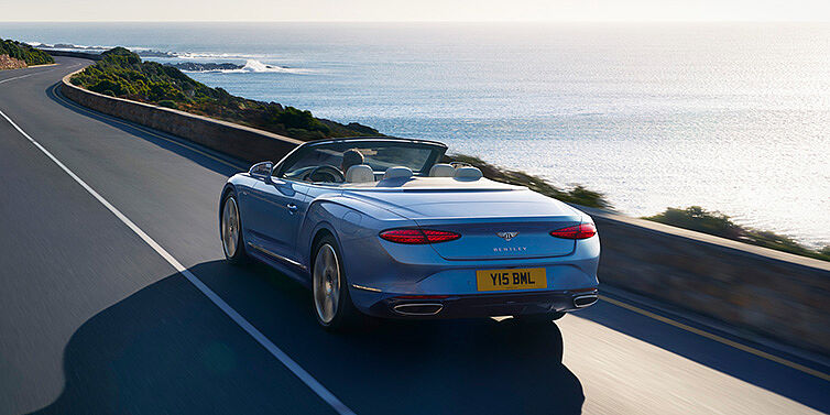 Bentley Johannesburg New Bentley Continental GTC Azure convertible rear view in Light Windsor blue paint with 22 inch ten spoke wheels driving dynamically on an ocean road in the sunshine
