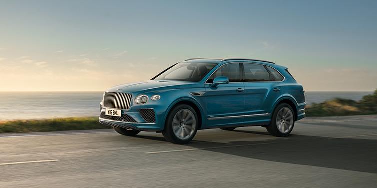 Bentley Johannesburg Bentley Bentayga Azure SUV in Topaz blue paint driving dynamically by the ocean with 22 inch 10 spoke directional wheels