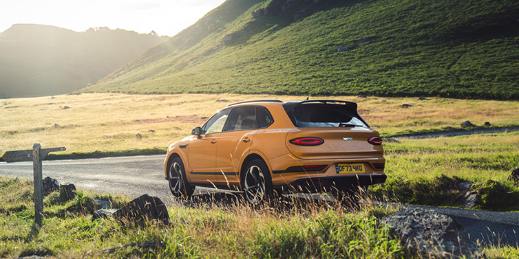 Bentley Johannesburg Bentley Bentayga S SUV rear three quarter in Sunburst Gold paint on a road surrounded by green hills