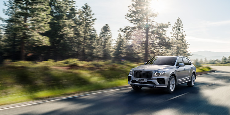 Bentley Johannesburg Bentley Bentayga SUV front three quarter in Moonbeam silver paint driving dynamically along a tree-lined road