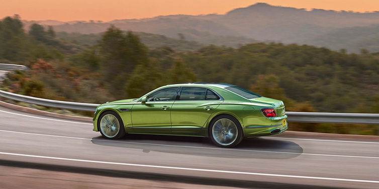 Bentley Johannesburg Bentley Flying Spur Speed sedan side profile in Tourmaline Green paint driving dynamically on a mountain road at sunset