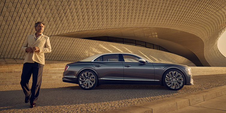 Bentley Johannesburg Bentley Flying Spur Mulliner sedan in Rose Gold over Magnetic duotone paint parked by a curved wall with person in suit jacket standing on the left